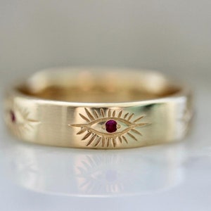 May include: A gold band ring with three engraved evil eyes. Each eye has a ruby gemstone in the centre.
