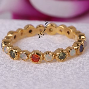 May include: A gold band ring featuring a series of alternating round gemstones in various colors including white, orange, and dark green. The metal setting has a scalloped edge around each stone. The text A1Jewells is visible on the ring.