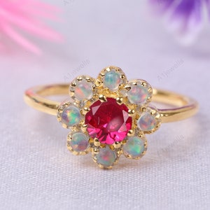 May include: A gold ring featuring a red gemstone surrounded by white opals in a flower design.