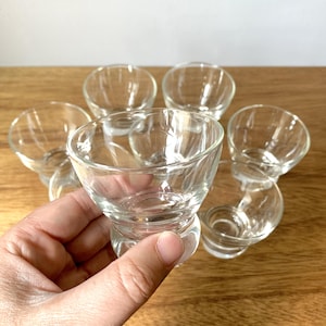 May include: A set of seven clear glass bowls, each featuring a wide, flared rim and a thick, rounded base. The bowls are transparent with a smooth, polished finish, designed with a distinct pedestal-style bottom that tapers into a circular foot.