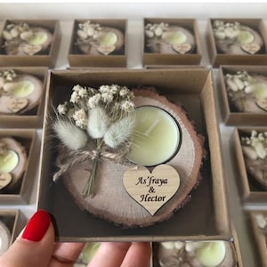 May include: A round wooden slice candle holder with a light yellow tea light candle, decorated with a small bouquet of dried white flowers and grasses, and a heart-shaped wooden tag engraved with the text As'fraya & Hector in a box.