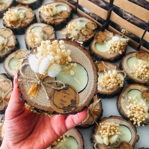 K&ouml;nnte beinhalten: Ein runder Kerzenhalter aus einer Holzscheibe mit einem hellgr&uuml;nen Teelicht, verziert mit einem kleinen Strau&szlig; aus getrockneten wei&szlig;en Blumen und Hasenschwanzgras, gebunden mit Bindfaden und einem runden braunen Papieranh&auml;nger mit dem Text "&Gamma;&iota;ά&nu;&nu;&eta;&sigmaf; & &Mu;&alpha;&rho;ί&alpha; 2021".