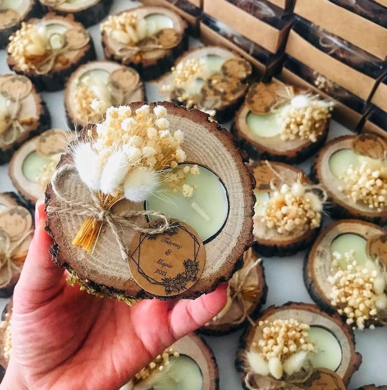 K&ouml;nnte beinhalten: Ein runder Kerzenhalter aus einer Holzscheibe mit einem hellgr&uuml;nen Teelicht, verziert mit einem kleinen Strau&szlig; aus getrockneten wei&szlig;en Blumen und Hasenschwanzgras, gebunden mit Bindfaden und einem runden braunen Papieranh&auml;nger mit dem Text "&Gamma;&iota;ά&nu;&nu;&eta;&sigmaf; & &Mu;&alpha;&rho;ί&alpha; 2021".