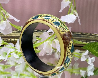 Può includere: Un braccialetto di legno giallo con interno nero e un motivo floreale in verde e marrone.