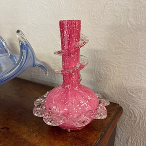 May include: A pink glass vase with a clear glass spiral design and a scalloped rim. The vase has a speckled finish.