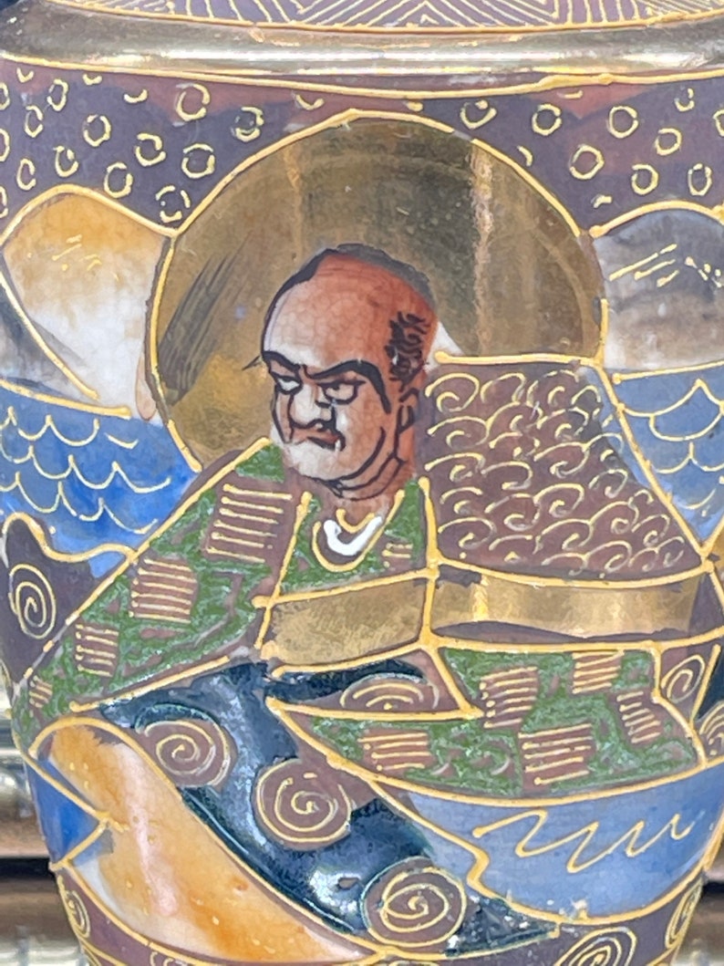 Puede incluir: Un jarr&oacute;n de cer&aacute;mica con un dise&ntilde;o dorado, azul y verde. El jarr&oacute;n presenta una imagen pintada de un hombre con barba y una t&uacute;nica estampada. El hombre est&aacute; rodeado de olas y nubes estilizadas.