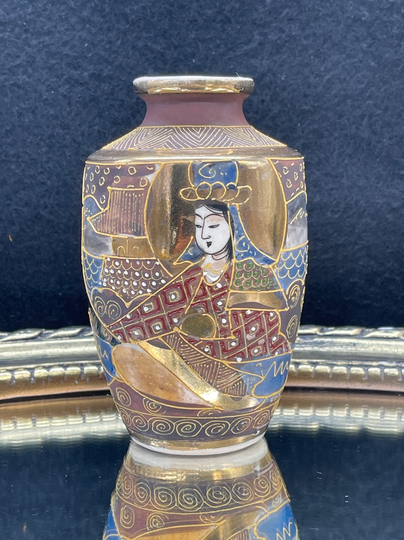 Puede incluir: Un peque&ntilde;o jarr&oacute;n de cer&aacute;mica pintado a mano con un dise&ntilde;o dorado y rojo. El jarr&oacute;n presenta una imagen detallada de una mujer con ropa tradicional japonesa.