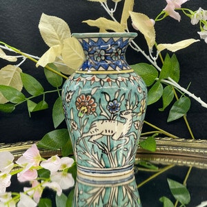 May include: A small, blue and white ceramic vase with a floral and animal design. The vase is decorated with a deer and floral patterns in shades of blue, green, red, and yellow.