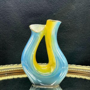 May include: A blue and yellow ceramic vase with a unique, abstract design. The vase has a gold trim and is perfect for displaying flowers or other decorative items.