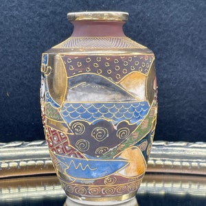 Puede incluir: Un peque&ntilde;o jarr&oacute;n de cer&aacute;mica decorativo con un borde dorado y dise&ntilde;os intrincados de inspiraci&oacute;n japonesa en tonos azules, marrones, dorados y blancos.