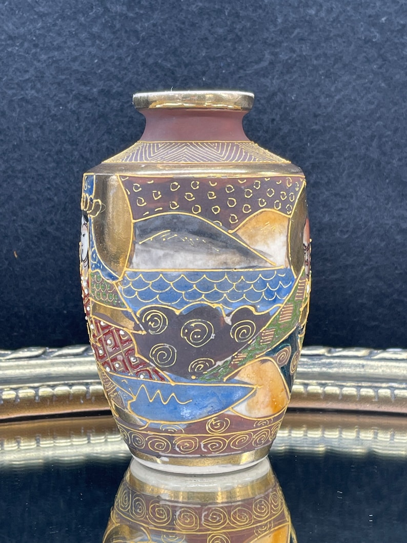 Puede incluir: Un peque&ntilde;o jarr&oacute;n de cer&aacute;mica decorativo con un borde dorado y dise&ntilde;os intrincados de inspiraci&oacute;n japonesa en tonos azules, marrones, dorados y blancos.