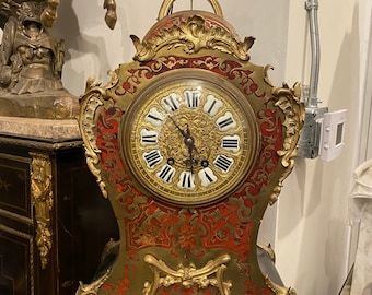 May include: A gold and red French mantel clock with ornate details and a Roman numeral clock face.