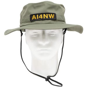 May include: Olive green boonie hat with a wide brim and a black chin strap. The hat features a rectangular patch with the text "AI4NW" in yellow letters.