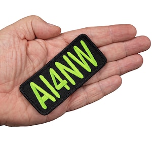 May include: A black rectangular patch with the neon green text "AI4NW" is shown. The patch is held in a hand against a white background. The text is in a bold, handwritten style.