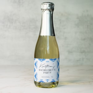 May include: A small bottle of sparkling wine with a white label that says "Kaitlin's Bachelorette Party Sedona, AZ" with a blue and white patterned design.