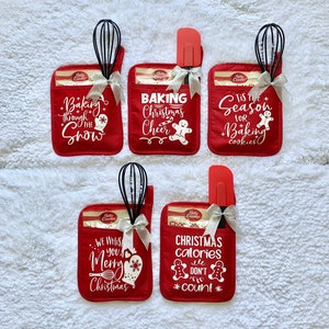 May include: Four red oven mitts with white text and images. The mitts are decorated with Christmas-themed sayings and images, such as "Baking Christmas Cheer" and "Christmas calories don't count". Each mitt is paired with a kitchen utensil, such as a whisk or spatula, and a Betty Crocker baking mix packet.