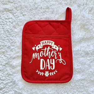 May include: Red quilted pot holder with white text that reads "Happy Mother's Day" with a small floral design.