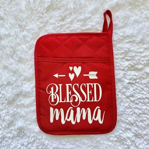 May include: Red quilted pot holder with a white arrow pointing to the right with three white hearts above it. The text "Blessed mama" is written in white cursive lettering.