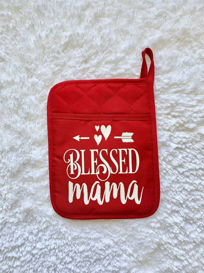 May include: Red quilted pot holder with a white arrow pointing to the right with three white hearts above it. The text "Blessed mama" is written in white cursive lettering.