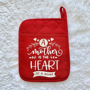May include: Red quilted pot holder with a white design that says "A mother is the heart of a home".