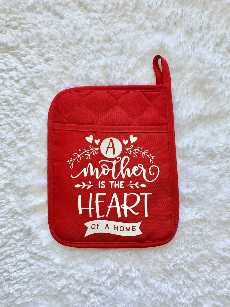May include: Red quilted pot holder with a white design that says "A mother is the heart of a home".