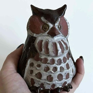 May include: A ceramic owl figurine with a brown body, red-brown facial features, and white accents. The owl has large, round eyes and a detailed, textured design. The figurine is a decorative item.