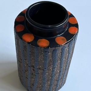 May include: A black and orange ceramic vase with a striped pattern and a ring of orange dots around the top.