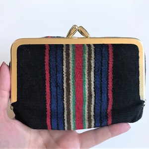 Può includere: Un piccolo porta monete in velluto nero con una cornice in metallo dorato e una chiusura. Il porta monete ha un motivo a strisce colorate in rosso, blu, verde e marrone.