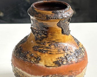 Może przedstawiać: Brązowy ceramiczny wazon z fakturowaną powierzchnią i kropkowanym szkliwem. Wazon ma szeroką podstawę i wąską szyjkę.