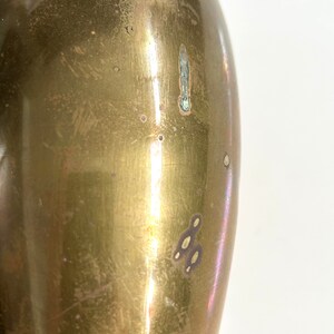 Puede incluir: Primer plano de un jarr&oacute;n de metal de color dorado con una superficie lisa y brillante. El jarr&oacute;n tiene una forma ligeramente ovalada y est&aacute; ligeramente abollonado en algunos lugares.