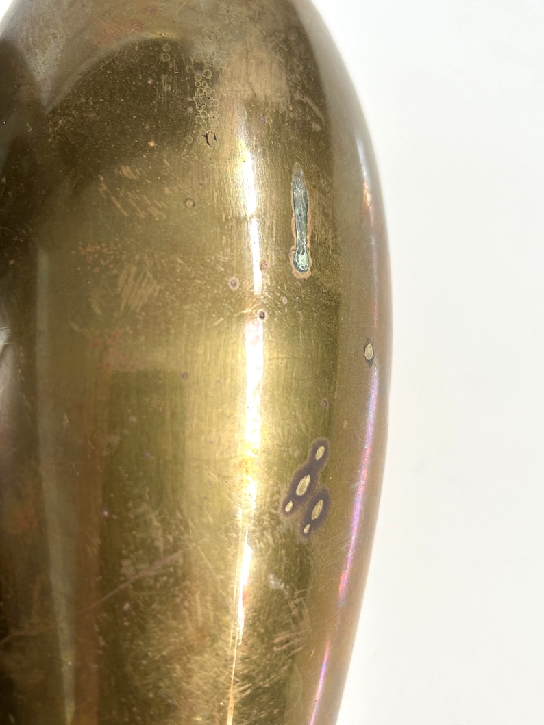 Puede incluir: Primer plano de un jarr&oacute;n de metal de color dorado con una superficie lisa y brillante. El jarr&oacute;n tiene una forma ligeramente ovalada y est&aacute; ligeramente abollonado en algunos lugares.