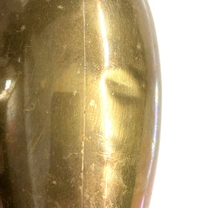 Puede incluir: Primer plano de un jarr&oacute;n de metal de forma ovalada de color dorado con una costura vertical en el centro. El jarr&oacute;n tiene una superficie lisa y pulida con algunos ara&ntilde;azos e imperfecciones.