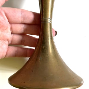 Puede incluir: Un jarr&oacute;n de metal dorado con una base acampanada y un cuello estrecho. El jarr&oacute;n tiene un acabado liso y pulido y una banda decorativa sutil alrededor del cuello.