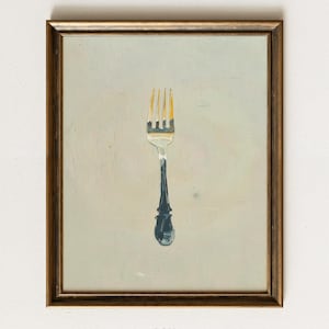 May include: A framed painting of a fork. The fork has a silver tine section with gold-colored tips and a dark blue handle. The painting is in a gold-colored frame and set against a light gray background.