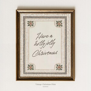 May include: A framed vintage Christmas print with the text "Have a holly jolly Christmas" in elegant script. The frame is a warm gold color, and the print has a mosaic-like border with holly accents.