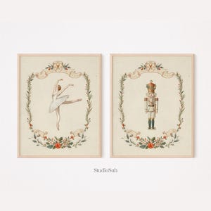 May include: Two framed prints featuring vintage illustrations. One depicts a ballerina in a white tutu, the other a nutcracker soldier. Both are framed with floral and ribbon accents, perfect for holiday decor.