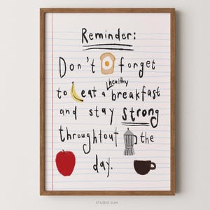 May include: A framed wall art print on lined paper featuring the text Reminder: Don't forget to eat a healthy breakfast and stay strong throughout the day. Illustrations include a piece of toast with an egg, a yellow banana, a red apple, a grey moka pot, and a black coffee cup.