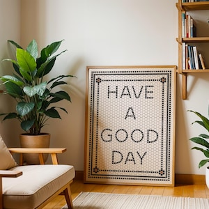 May include: A framed print with a white background and black text that reads "HAVE A GOOD DAY". The text is on a tiled background with a black border. The print is hanging on a white wall.