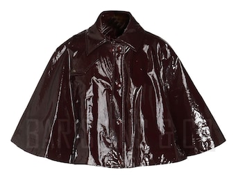 May include: A glossy, burgundy cape with a wide collar and button closure. The outerwear has a shiny, patent leather-like finish, reflecting light. The cape's design includes a small pocket detail on the chest.