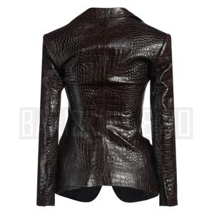 May include: A dark brown blazer with a crocodile skin texture. The blazer has a notched lapel, long sleeves, and a two-button closure. The back of the blazer is visible, showcasing the tailored fit and textured pattern.