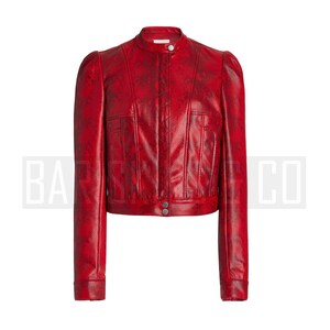 May include: A red, cropped jacket with a snakeskin pattern. The jacket features a stand-up collar, long sleeves, and a button closure. The jacket has a fitted silhouette and is made of a textured material.