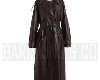 May include: A long, dark brown trench coat with a double-breasted design. The coat features a belt at the waist, epaulettes on the shoulders, and a classic collar. The coat is made of a smooth, leather-like material.