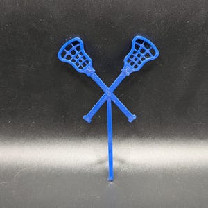 May include: Two blue lacrosse sticks are crossed over each other. The sticks are made of plastic and have a net at the end.
