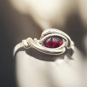 May include: A silver ring with a red gemstone set in a wire-wrapped design.