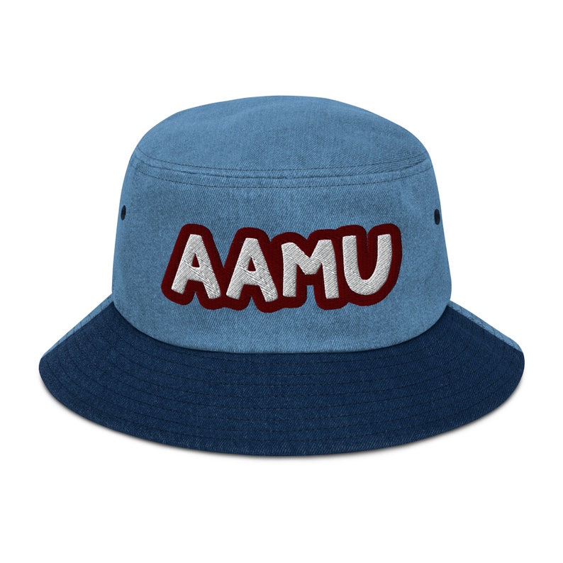 以下が含まれることがあります： 青いデニムのバケットハットで、コントラストの効いた濃い青色のつばが付いています。ハットには、「AAMU」と刺繍された白と赤のロゴがあります。