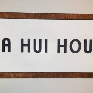 May include: A wooden sign with a brown frame and white background. The sign says "A HUI HOU" in black letters.