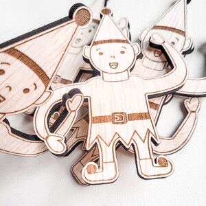 May include: A set of four wooden elf ornaments, each with a different pose and expression. The elves are wearing pointy hats and have a whimsical, festive look.