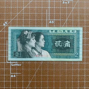 May include: A light green Chinese banknote featuring two women in profile. The note has the text "中国人民银行" at the top and the number "2" in two corners. The note is rectangular and has a decorative border.