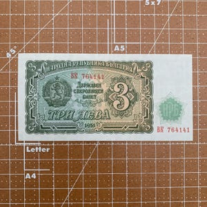 May include: A green and brown Bulgarian banknote with the text "НАРОДНА РЕПУБЛИКА БЪЛГАРИЯ" and "ТРИ ЛЕВА" printed on it. The banknote features a lion and the number "3" in the center.