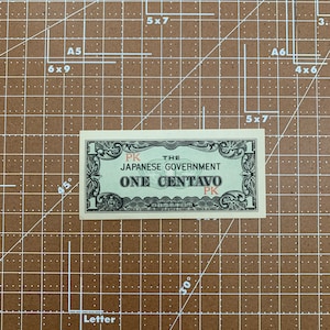 May include: A green and white paper banknote with the text "THE JAPANESE GOVERNMENT ONE CENTAVO" printed in red and black. The banknote has a border of ornate floral designs and the text "PK" printed in red on both sides.